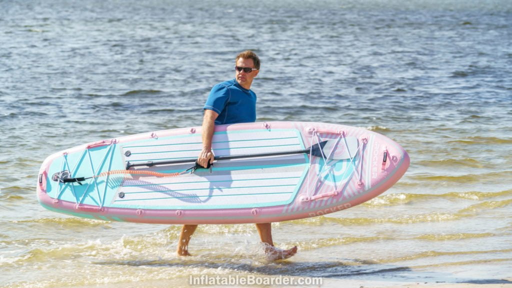A man carrying the pink board out of the ocean.