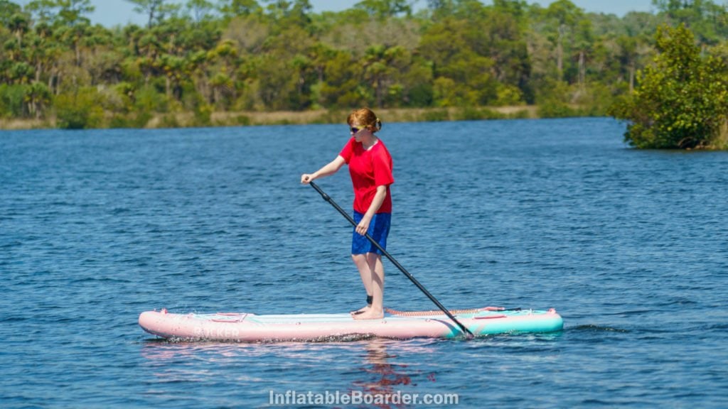 Side shot of a teen woman paddling the board on calm water.