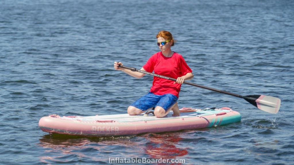 A teen kneeling on the board to paddle for extra stability.