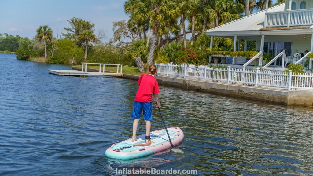A teen paddling the pink board towards shore.