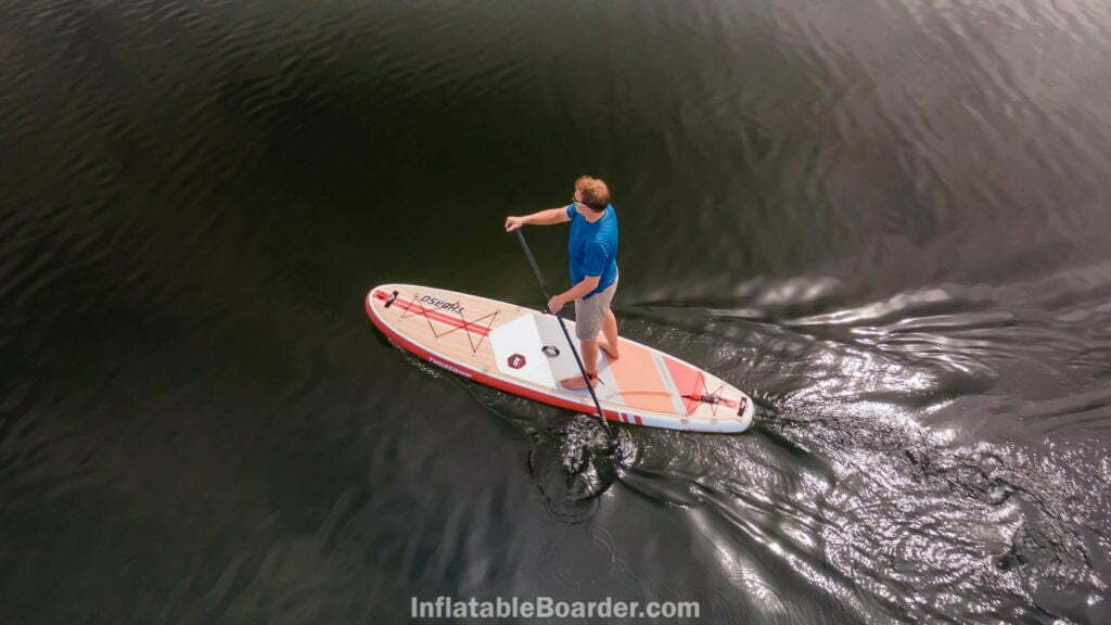 Paddling the crimson board from above on smooth water.