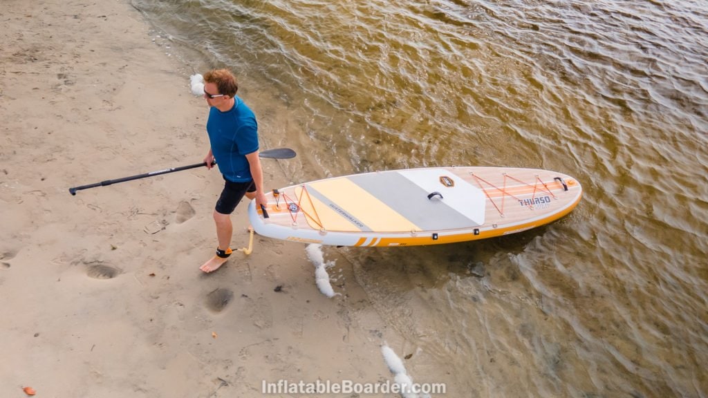 Carrying the board out of the ocean to a beach, viewed from above.
