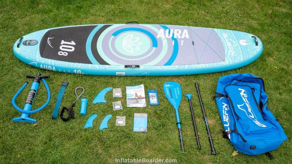 Overview of the Aura Fit's accessories, including a basic pump, compression strap, SUP leash, repair kit, 3 fins, fiberglass paddle, bag, phone case, warranty card.
