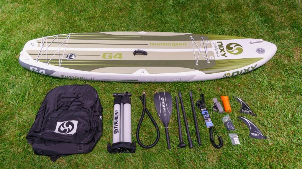 Unboxed NIXY Huntington G4 with accessories, including compact bag, dual chamber pump, 4-piece paddle, coiled SUP leash, compression strap, repair kit, and 2 fins.