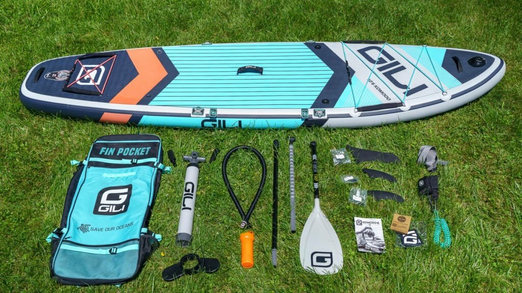 Unboxing the teal GILI Komodo accessories, including basic bag, compact pump, carbon TRP paddle, 3 fins, repair kit, SUP leash, compression strap, and documentation.